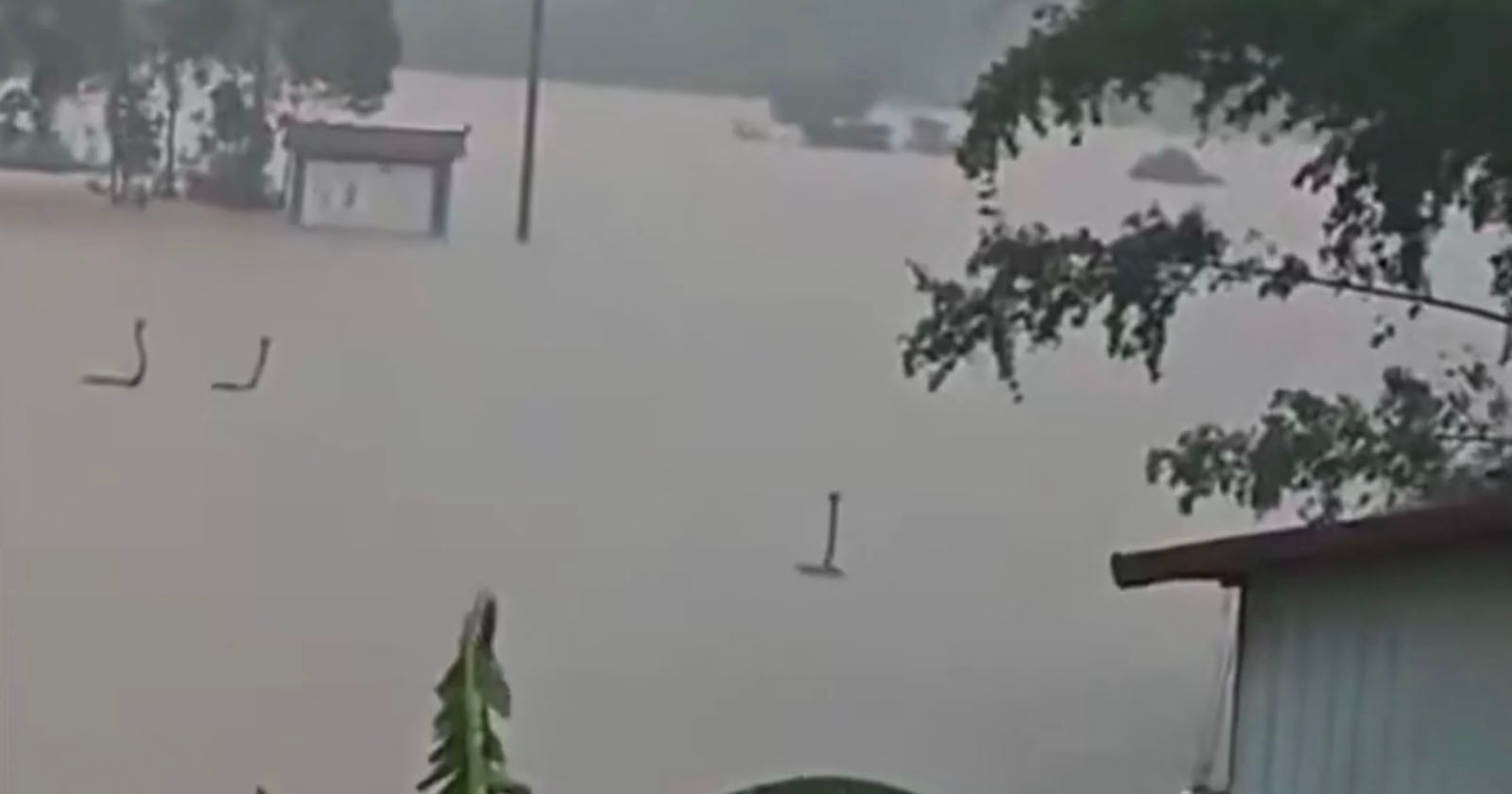 Flooded area with rooftops and trees barely visible above the water. Only the tops of structures and some plants are seen, highlighting the severity of the flooding.