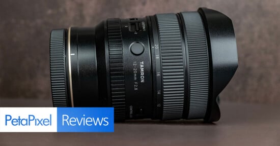 A Tamron 20-40mm camera lens with a lens hood sits on a brown surface. Text at the bottom left reads “PetaPixel Reviews.”.