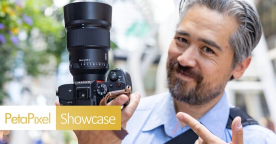 A man with gray hair and a beard smiles and points at a Sony camera with a large lens. The image features banners reading “PetaPixel” and “Showcase” in the bottom left corner.