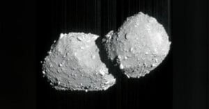 A grayscale image shows two rocky, irregularly shaped asteroids or space objects floating close together against a dark background, resembling a contact binary or two joined celestial bodies.