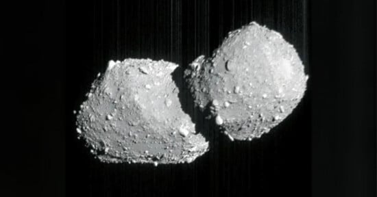 A grayscale image shows two rocky, irregularly shaped asteroids or space objects floating close together against a dark background, resembling a contact binary or two joined celestial bodies.