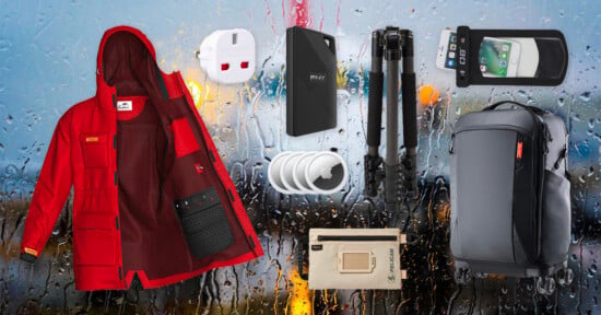 A red jacket, a white travel adapter, a PNY power bank, a tripod, a waterproof phone pouch, three AirTags, a small tan Pelican pouch, and a black rolling suitcase are arranged against a rainy window background.