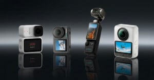 Four compact action cameras stand upright on a reflective surface, each with a display screen showing outdoor scenes. The background is dark and gradient.