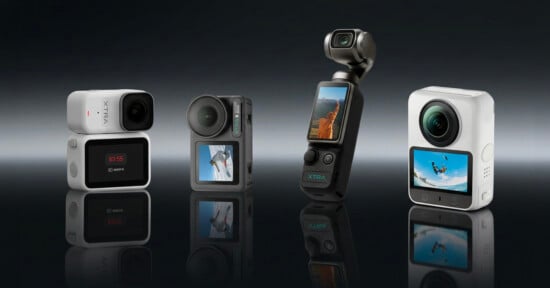 Four compact action cameras stand upright on a reflective surface, each with a display screen showing outdoor scenes. The background is dark and gradient.
