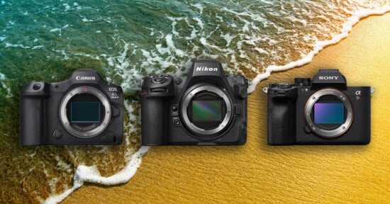 Three mirrorless cameras—Canon, Nikon, and Sony—are displayed side by side on a sandy beach with ocean waves in the background.