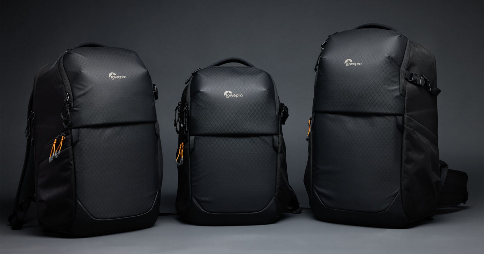 Three black Lowepro backpacks of varying sizes stand side-by-side against a plain gray background.