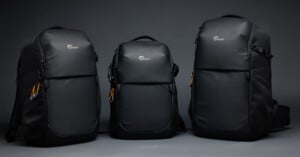 Three black Lowepro backpacks of varying sizes stand side-by-side against a plain gray background.