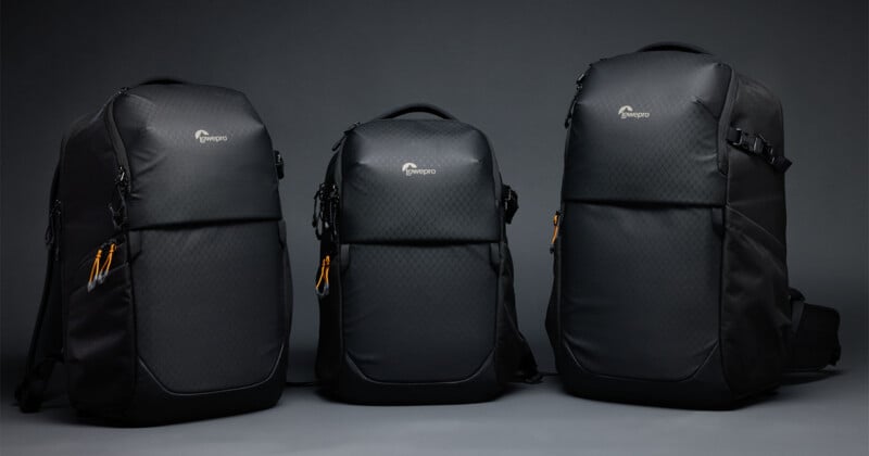 Three black Lowepro backpacks of varying sizes stand side-by-side against a plain gray background.