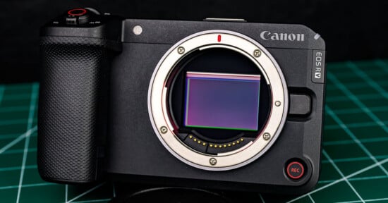 A Canon EOS RM mirrorless camera body with its lens removed, showing the sensor, placed on a green cutting mat background.