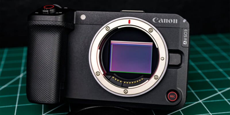 A Canon EOS RM mirrorless camera body with its lens removed, showing the sensor, placed on a green cutting mat background.
