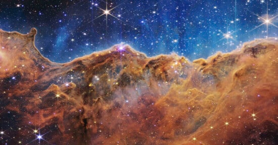 Colorful nebula with bright stars scattered across a vivid blue and orange cosmic cloud, resembling a mountainous landscape in outer space.