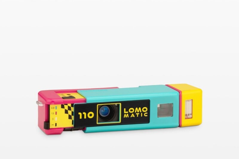 A colorful, rectangular 110 film camera with a sliding teal body, pink ends, and a yellow flash unit, featuring a black lens panel labeled "110 LOMO MATIC.