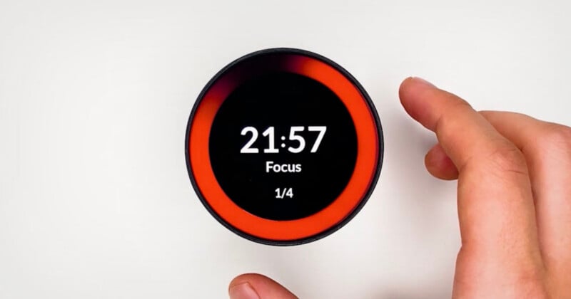 A hand adjusts a round digital timer displaying "21:57 Focus 1/4" on its screen, surrounded by a red progress ring, against a white background.
