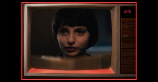 A close-up of a young person with short dark hair appears on an old-fashioned television screen, which displays the channel as UHS. The TV has wood paneling and red lighting around the edges.