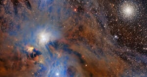 Colorful nebula with swirling blue, orange, and brown clouds, stars scattered throughout, and a dense cluster of bright stars in the upper right corner against the dark backdrop of space.