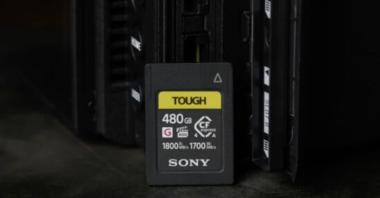 A Sony Tough CFexpress Type A memory card with 480GB capacity is standing upright in front of an electronic device, possibly a camera or card reader, on a dark surface.