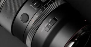 A close-up view of a camera lens barrel featuring an aperture ring with f-stop markings, an AF/MF switch, a customizable button, and a click on/off switch.