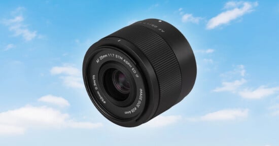 A black camera lens floating against a bright blue sky with scattered white clouds.