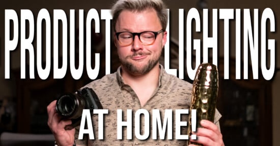 A man in glasses holds a camera and a golden object, standing in front of large text that says "PRODUCT LIGHTING AT HOME!" The background is softly lit and out of focus.
