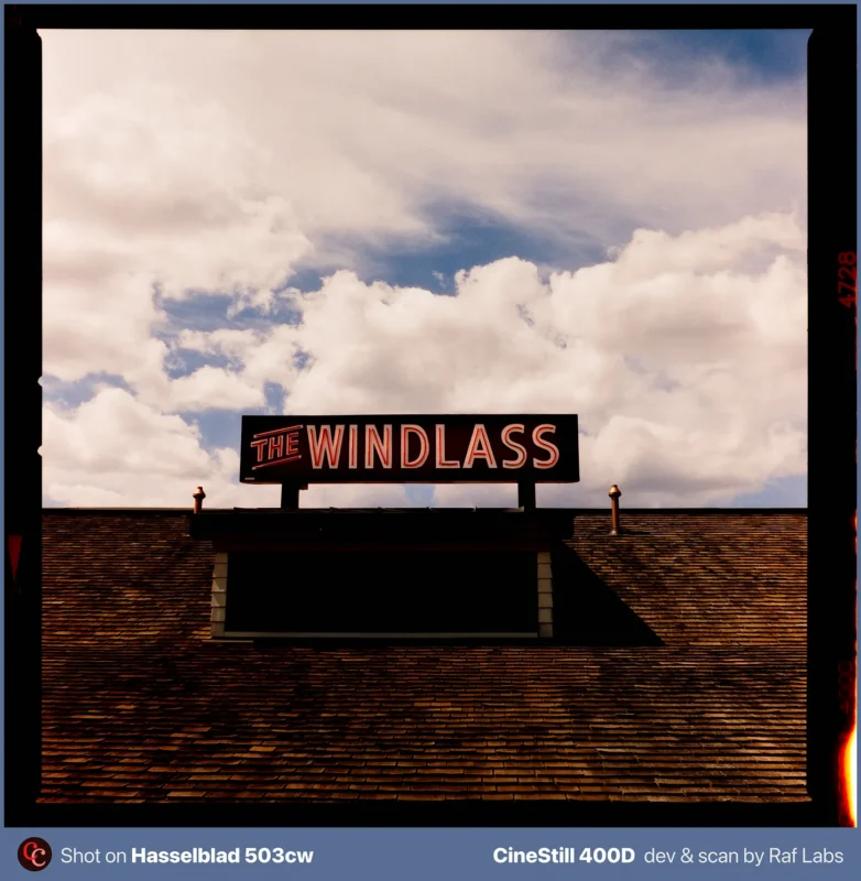 A sign reading "THE WINDLASS" sits atop a shingled roof against a cloudy blue sky.