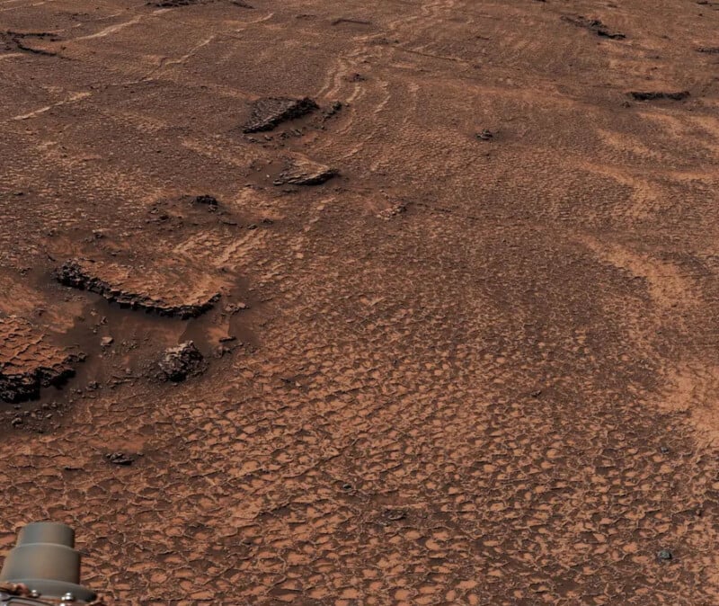 A high-angle view of a rocky, reddish Martian landscape featuring a distinct pattern of polygonal cracks in the ground.