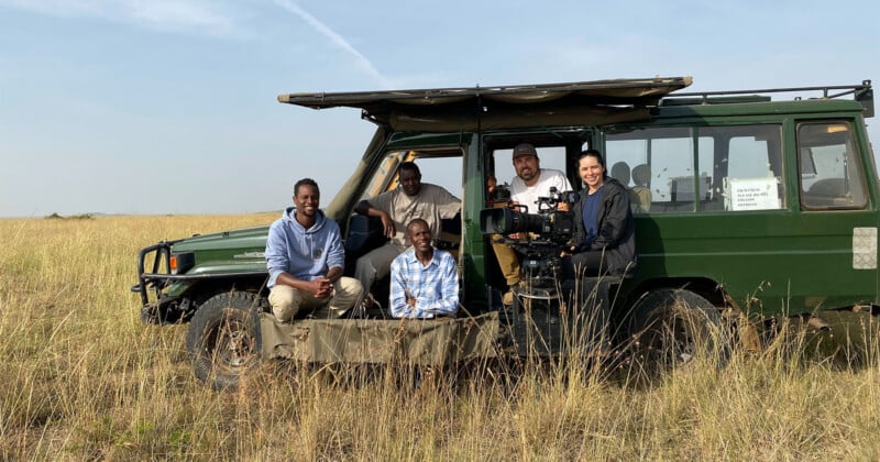 Five people pose for a group photo inside and around a green safari vehicle parked in a grassy field.