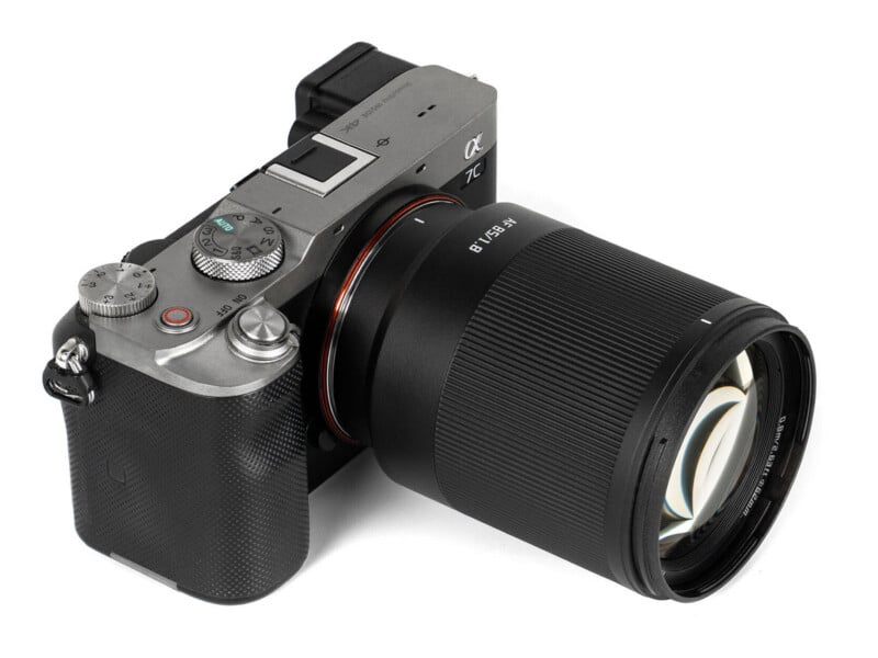 A silver and black mirrorless camera with an 85mm f/1.8 lens attached, viewed from a high angle against a white background.