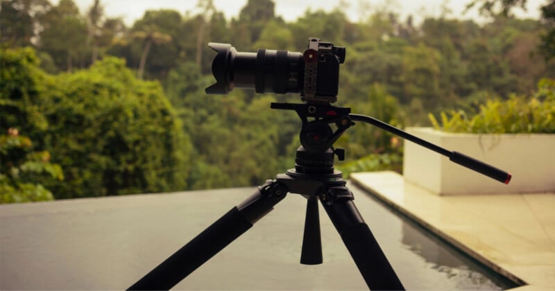 A camera mounted on a tripod stands overlooking a swimming pool with a lush, green forest in the background.