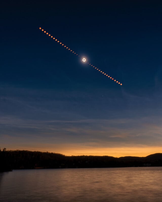 A composite image shows a solar eclipse progressing in a diagonal line across a twilight sky above a calm lake.