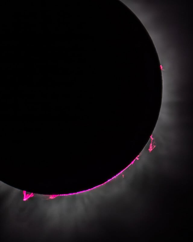 A total solar eclipse showing the moon silhouetted against the sun, with bright pink solar prominences visible along the edge.