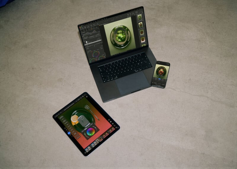 A laptop, a tablet, and a smartphone are arranged on a concrete floor, all displaying photo editing software with images of food.