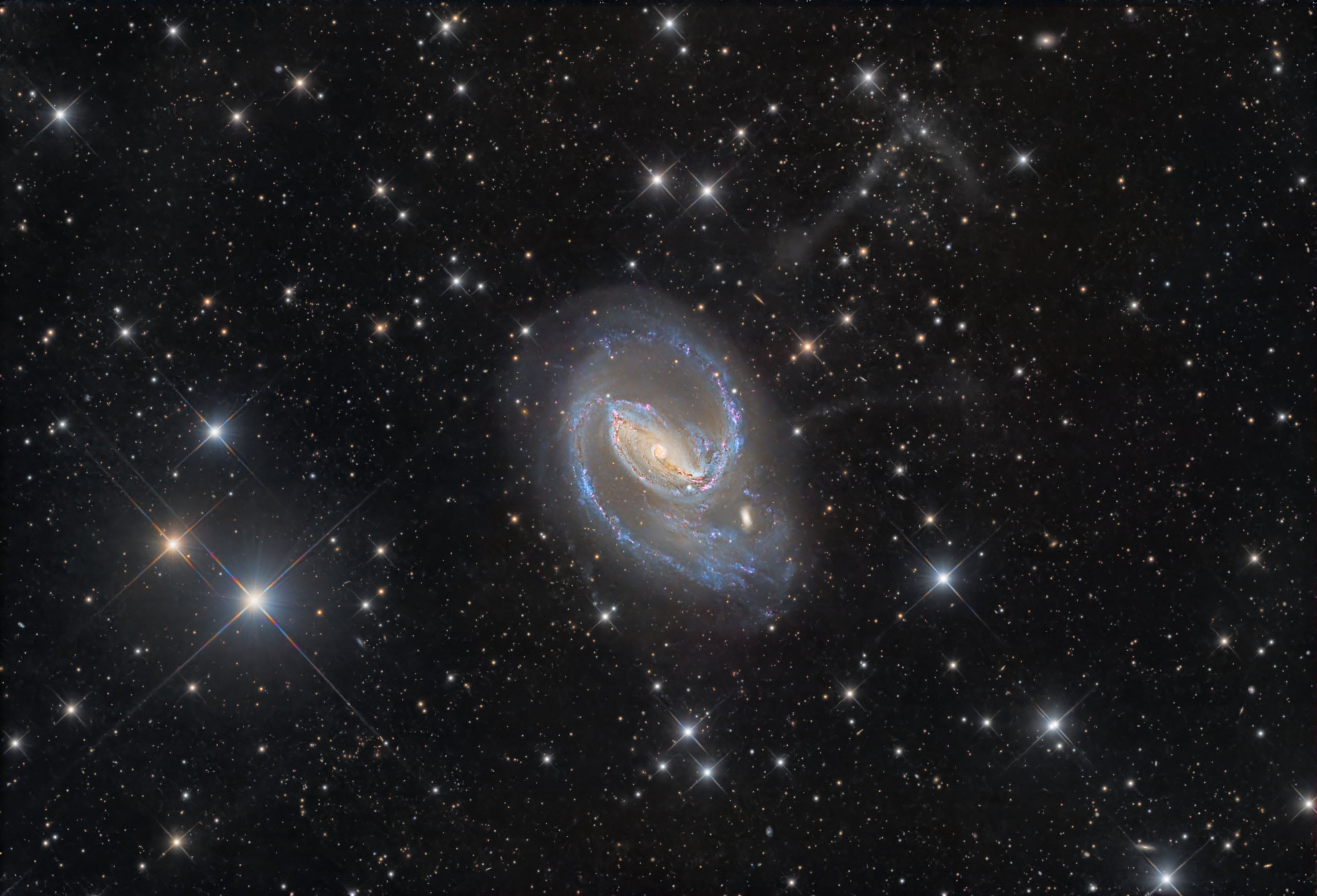 A barred spiral galaxy with bright blue star-forming regions and a glowing central bar sits against a dense field of stars.