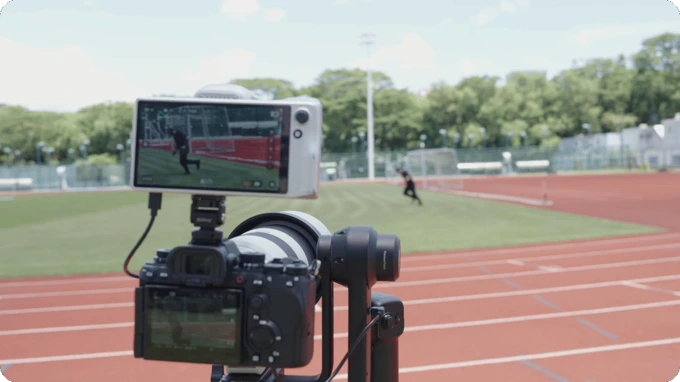 A camera mounted on a gimbal records a person running across a track and field facility.