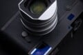 A black Leica rangefinder camera with a silver lens and a square hood sits on a dark surface.