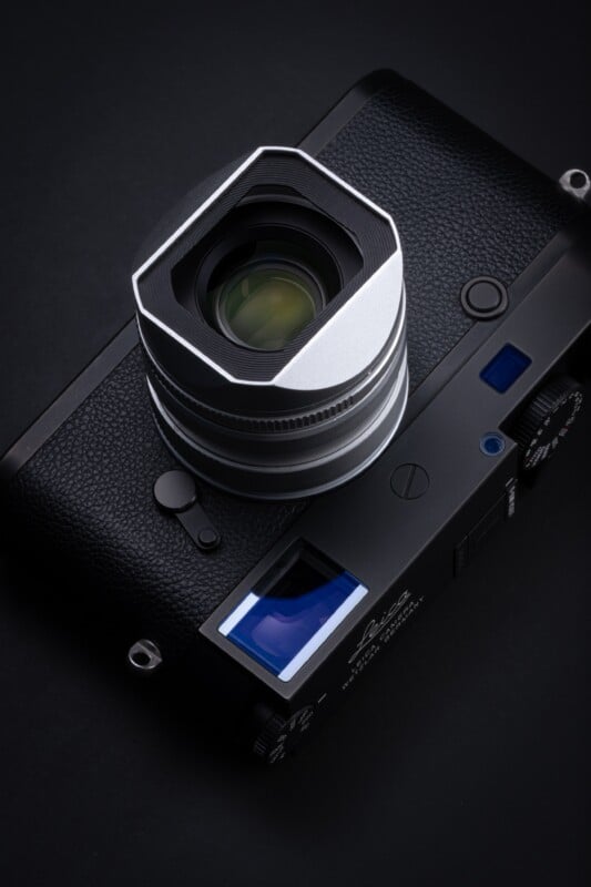 A black Leica rangefinder camera with a silver lens and a square hood sits on a dark surface.