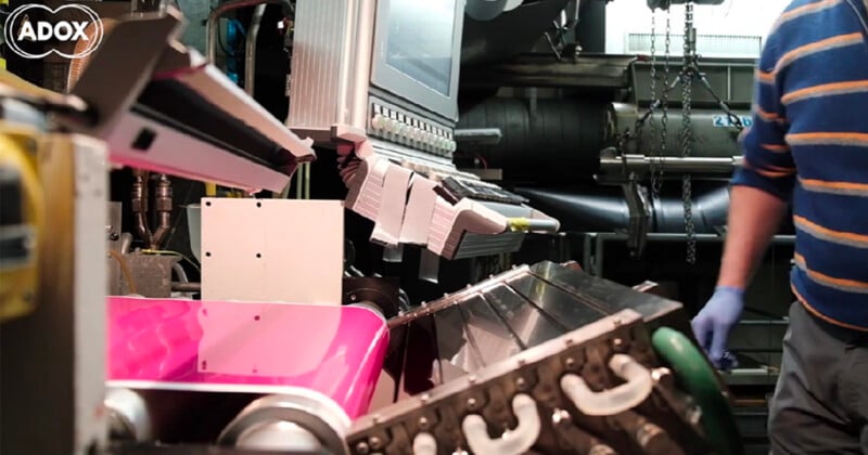 A person wearing blue gloves and a striped sweater operates industrial machinery processing a bright pink material.