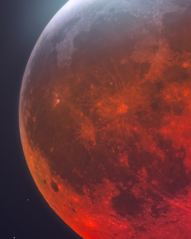 A close-up view of a lunar eclipse showing the moon's surface in deep red hues with a bright, illuminated crescent edge.