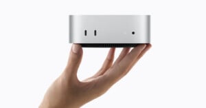 A hand holds a small, silver, cylindrical computer with two USB-C ports and a status light on its front face.