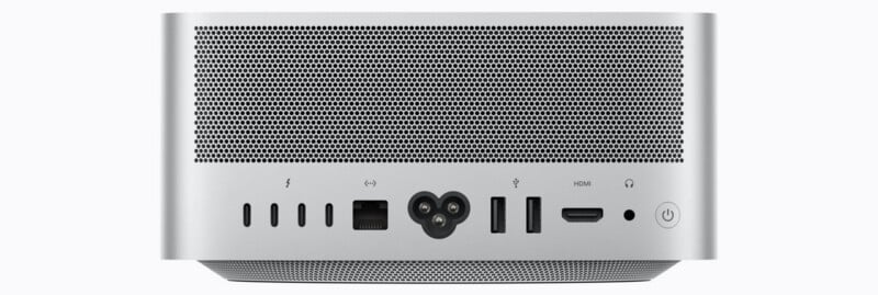 The back panel of a silver computer features a large ventilation grille above a row of ports, including four Thunderbolt ports, an Ethernet port, a power input, two USB-A ports, an HDMI port, a headphone jack, and a power button.