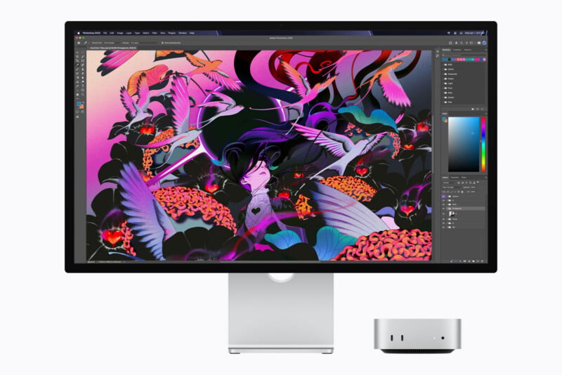A silver desktop computer and monitor display a vibrant digital illustration of a figure surrounded by birds and abstract shapes in Adobe Photoshop.