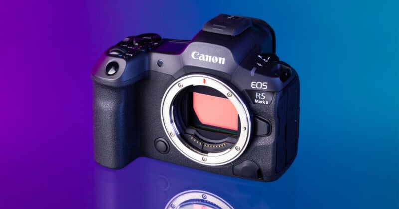 A black Canon EOS R5 Mark II mirrorless camera body sits on a reflective surface against a purple and blue gradient background.