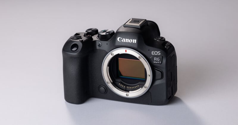 A black Canon EOS R6 Mark II mirrorless camera body sits on a light gray surface, showing the lens mount and sensor.