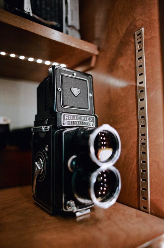 A vintage Rolleiflex twin-lens reflex camera sits on a wooden shelf next to a metal adjustable shelving track.