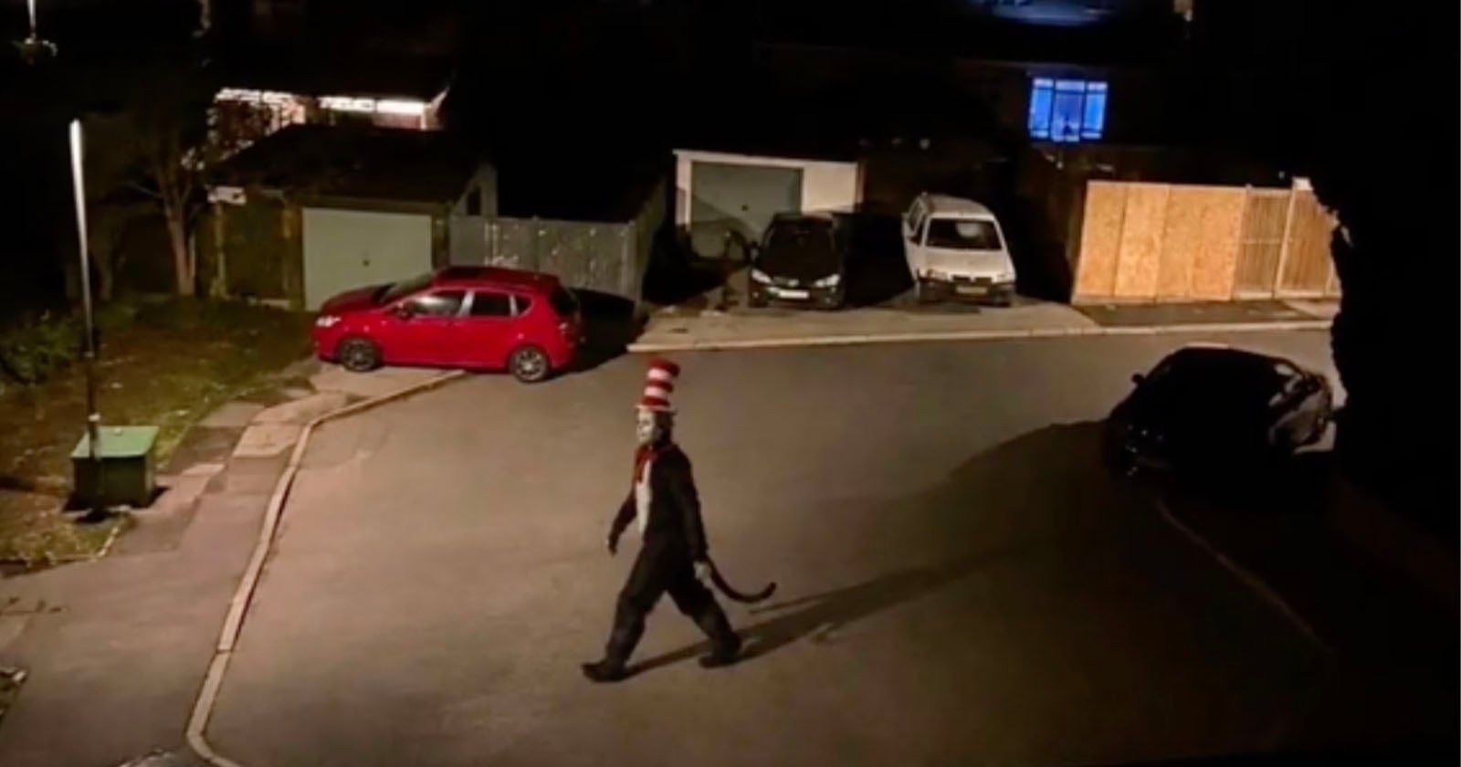 A person dressed in a Cat in the Hat costume walks across a residential street at night.