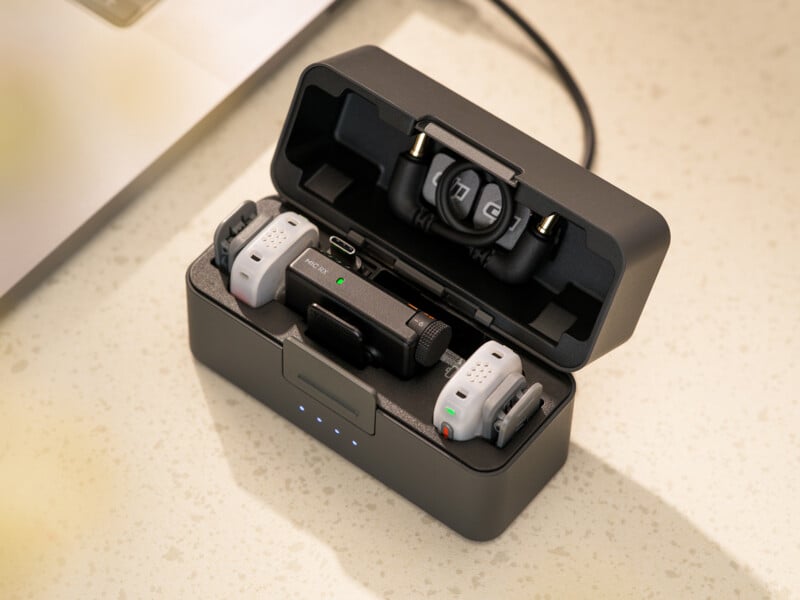 A DJI wireless microphone charging case is open, containing a receiver, two transmitters, and a coiled audio cable.