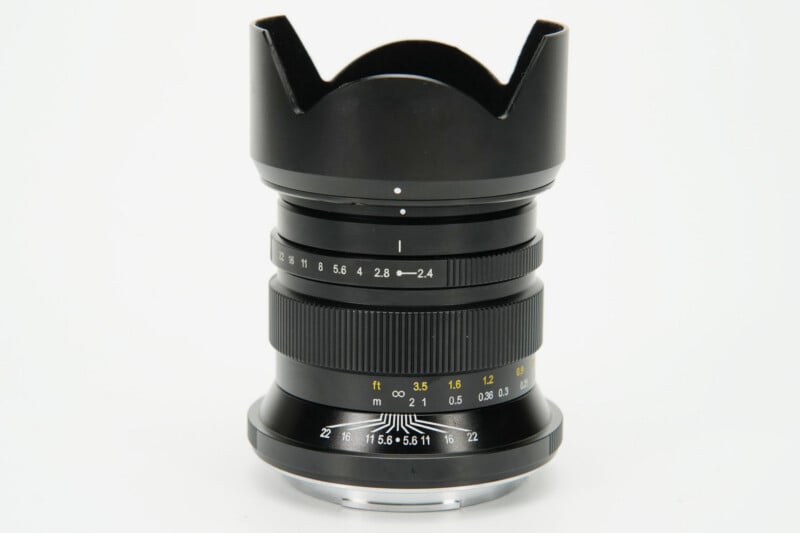 A black manual focus camera lens with a petal-shaped hood, aperture ring, and distance scale markings in feet and meters.