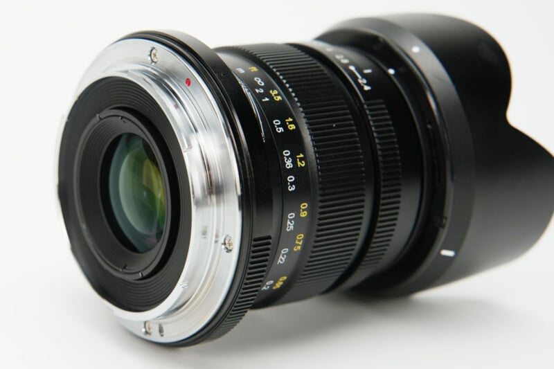 A black camera lens with a silver metal mount, focus distance markings in feet and meters, and a petal-shaped lens hood.