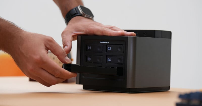 A person's hands insert a drive tray into a four-bay Digiera storage enclosure on a wooden desk.