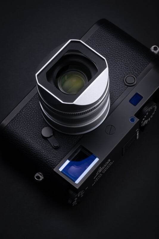 A black Leica rangefinder camera with a silver lens and a square lens hood sits on a dark surface.