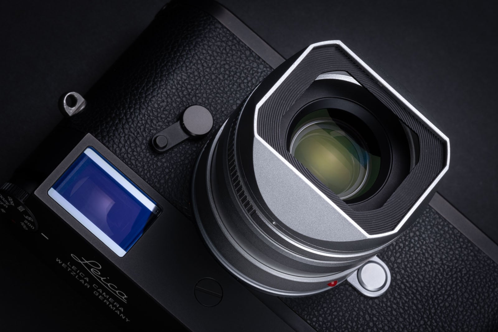 A top-down view of a black Leica camera featuring a silver lens with a square hood and a small rectangular display screen.